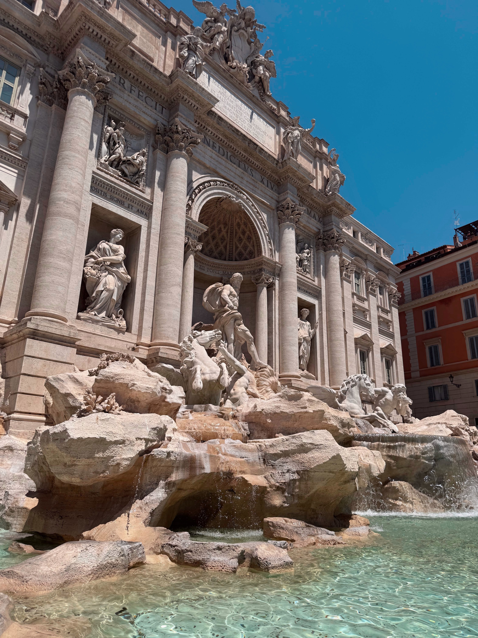 Up close view of the Trevi Fountain in Rome. A large marble fountain that looks like a building with statues and rocks that spill water out into the fountain below.