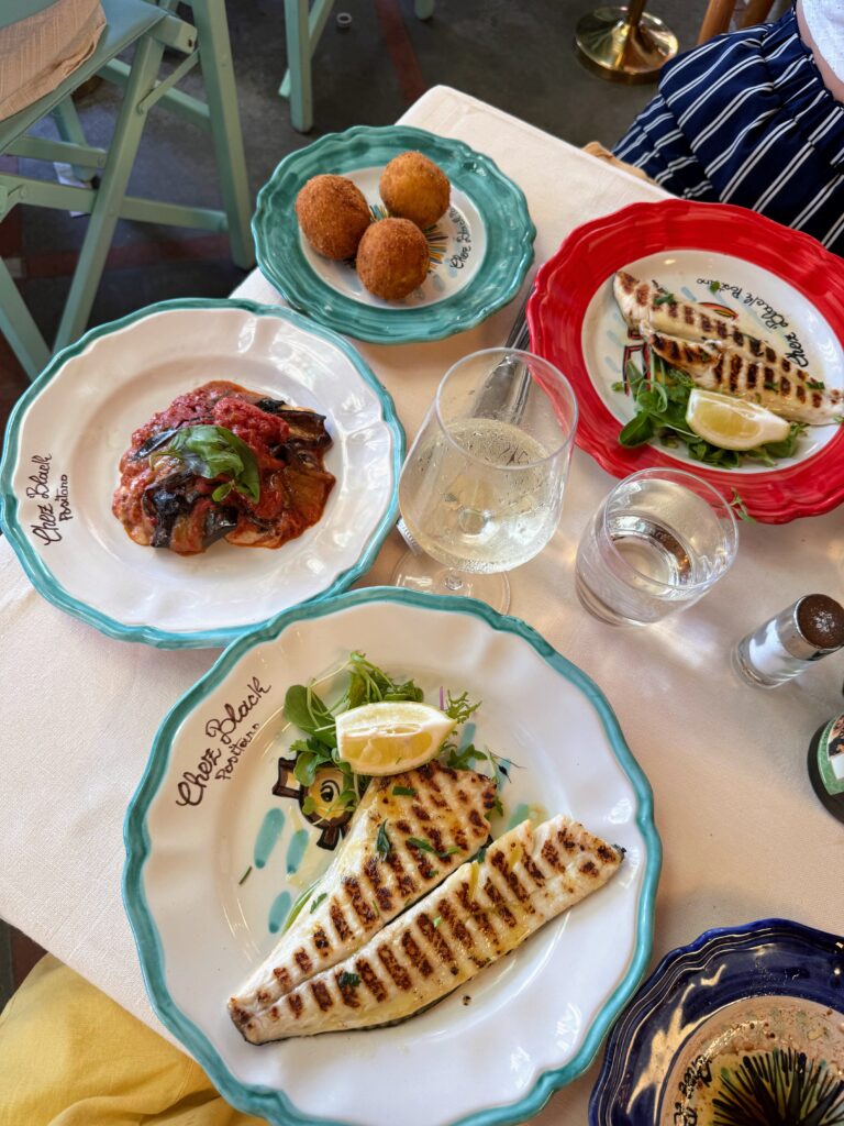 View of table with plates of fish, eggplant, fried rice balls and wine.
