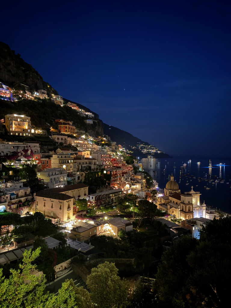 View of Positano at night, looking out onto the sea and the brightly lit buildings on the mountain.