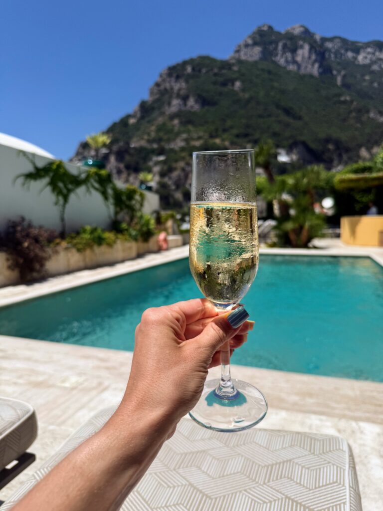 Woman's arm holding up a champagne glass with a rooftop pool and mountains in the background.