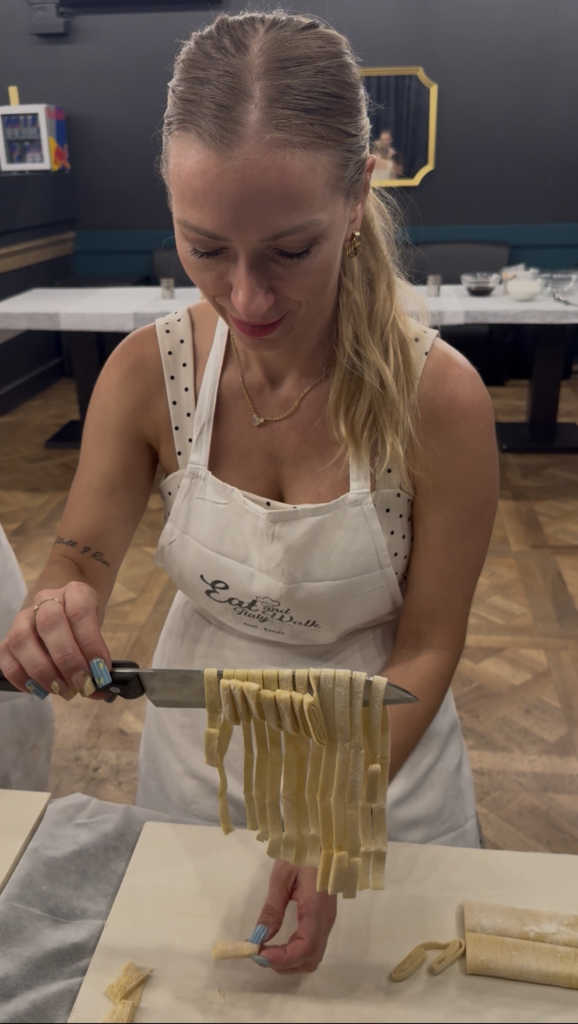 Woman making pasta from scratch. Holding a knife with pasta wrapped around it over a cutting board at a cooking class.