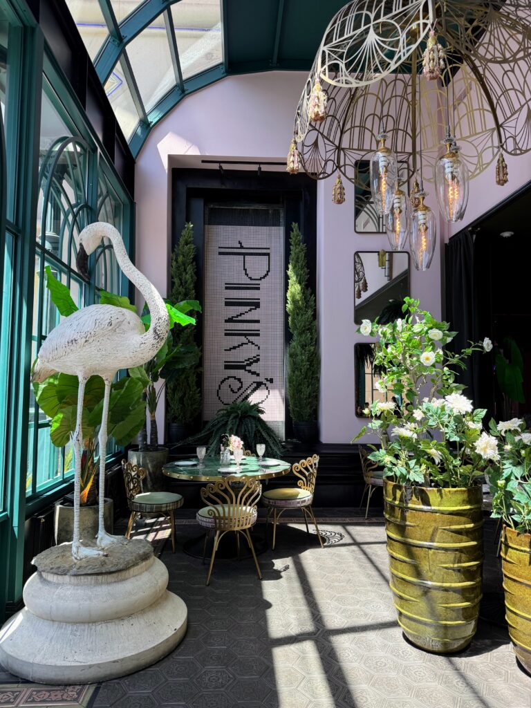 Lisa Vanderpump's restaurant Pinky's in Las Vegas. The walls are light pink with deep green window trim and plants everywhere.